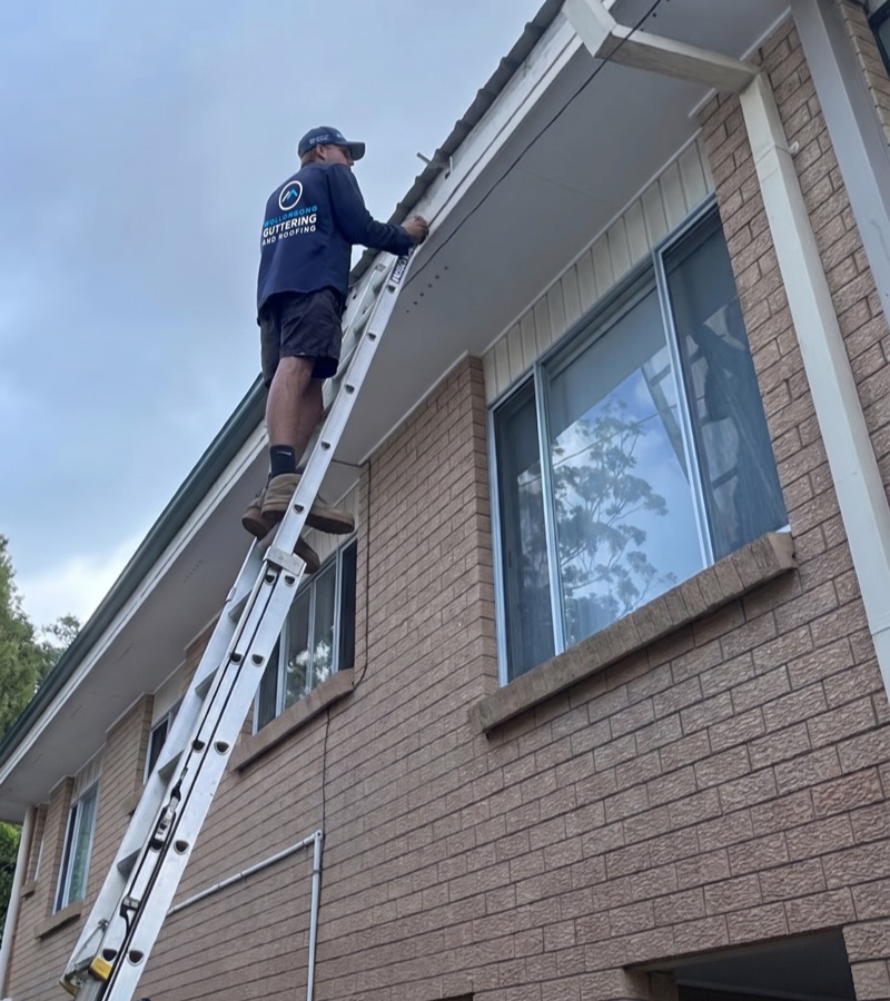 Roofer on a ladder assessing storm damaged gutters and roof
